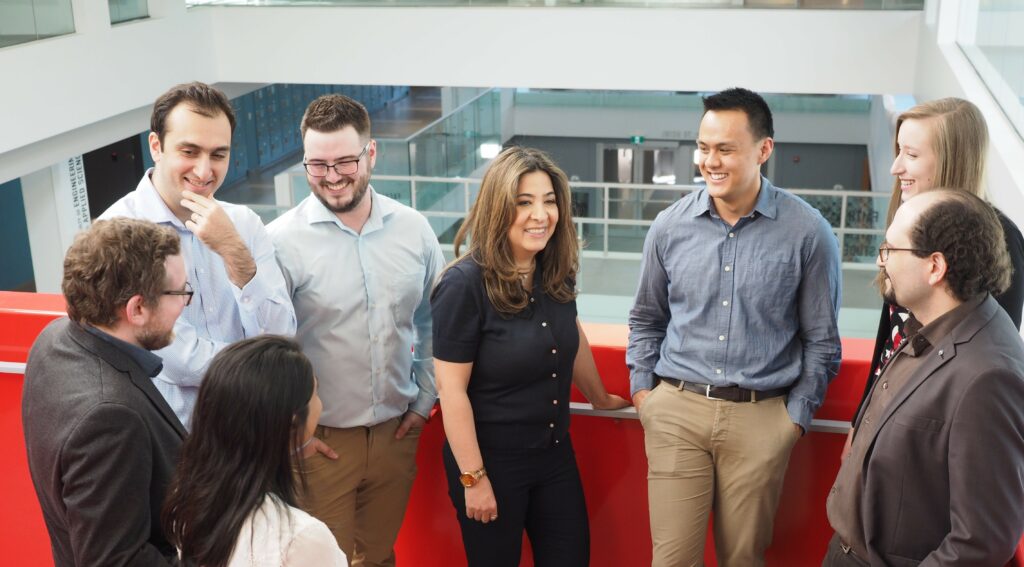 Dr. Parvin Mousavi standing in a group of researchers from her team on the second floor of Mitchell Hall. Everyone is smiling and engaged in conversation.