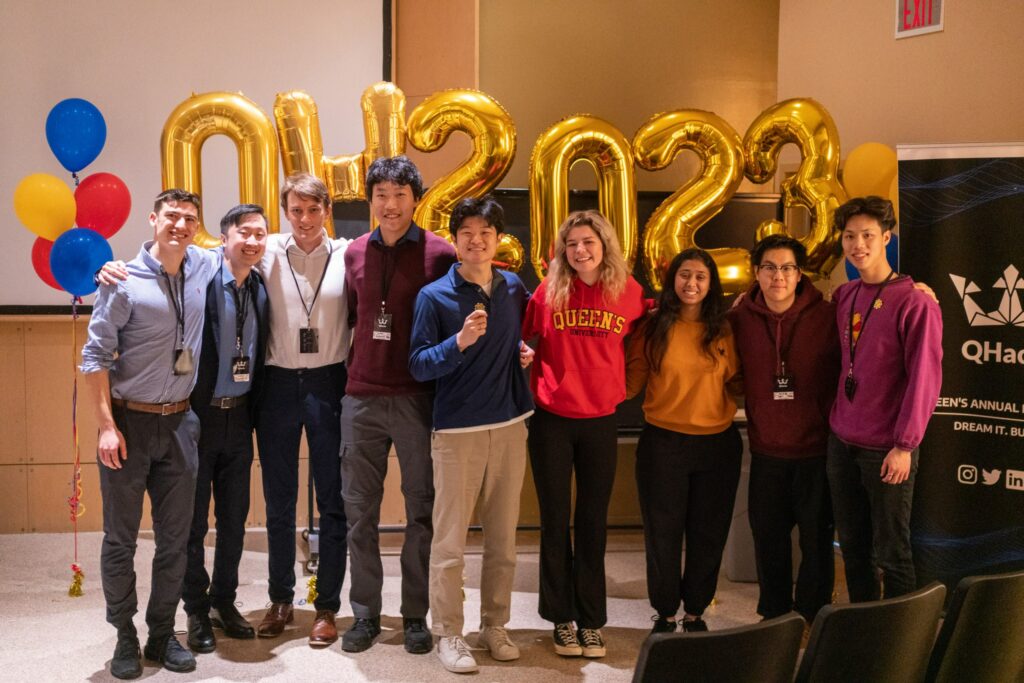 captains of winning teams posing for a group photo in front of inflatable golden balloons that spell out QHacks 2023